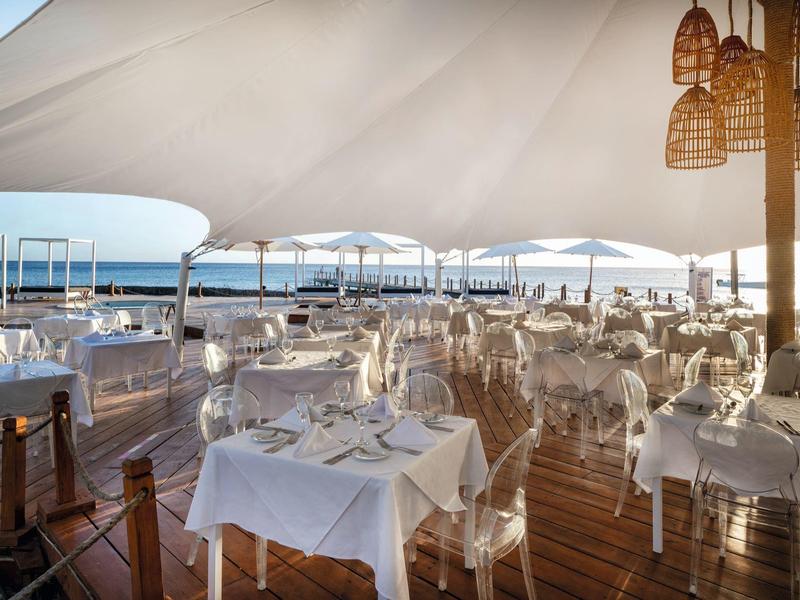 Restaurant élégant au bord de l'eau avec des tables et des chaises blanches sous un grand auvent.