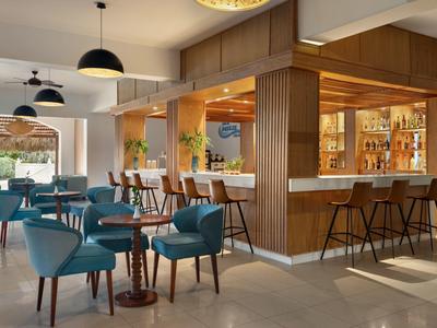 Área moderna de bar de hotel con sillas azules, detalles en madera y lámparas colgantes elegantes.