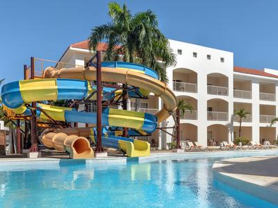 Parque acuático con toboganes coloridos junto a un hotel bajo un cielo azul despejado.