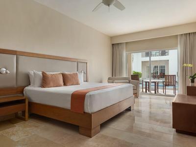 Habitación de hotel moderna con cama grande, área de estar y balcón con vista al exterior.