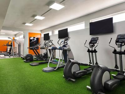 Nowoczesna siłownia z bieżniami, orbitrekami i maszynami siłowymi na zielonej sztucznej trawie.