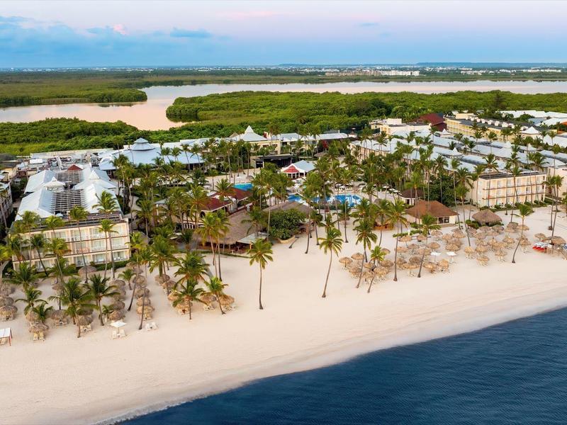 Vista aérea de un resort con palmeras en una playa de arena blanca junto al mar tranquilo.