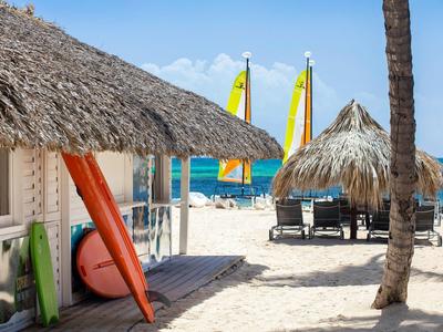 Strand met rieten hutten, palmbomen en zeilboten bij de zee op de achtergrond.