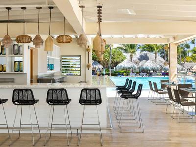 Moderner Außenbarbereich mit Barhockern, Tischen und Blick auf einen Pool und Garten.