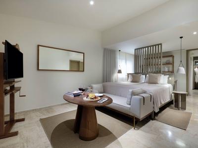 Modern ingericht hotelkamer met groot bed, bank, tv en houten tafel.