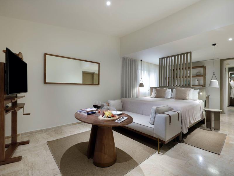 Modern ingericht hotelkamer met groot bed, bank, tv en houten tafel.