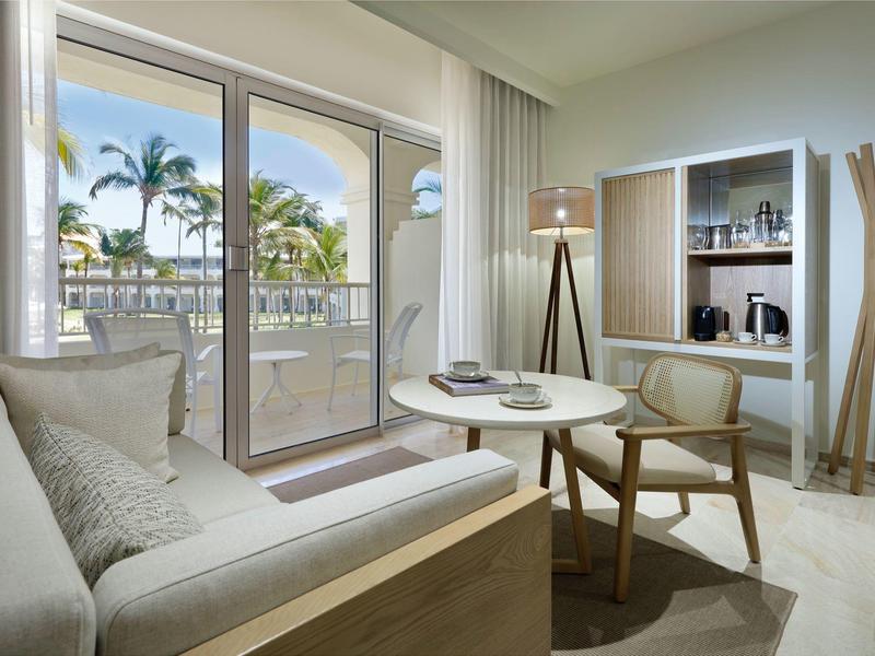 Moderne hotelkamer met zithoek en balkon met uitzicht op tropisch landschap.