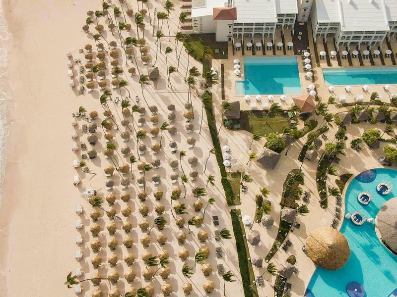 Luchtfoto van een strandhotel met parasols, twee zwembaden en aangrenzend zandstrand.