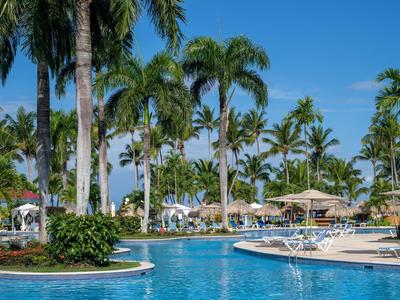 Großer Pool mit Palmen und Liegestühlen unter klarem blauen Himmel in einem Resort.