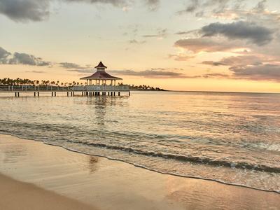 Strand mit sanften Wellen, Steg und Pavillon im goldenen Licht eines ruhigen Sonnenuntergangs.