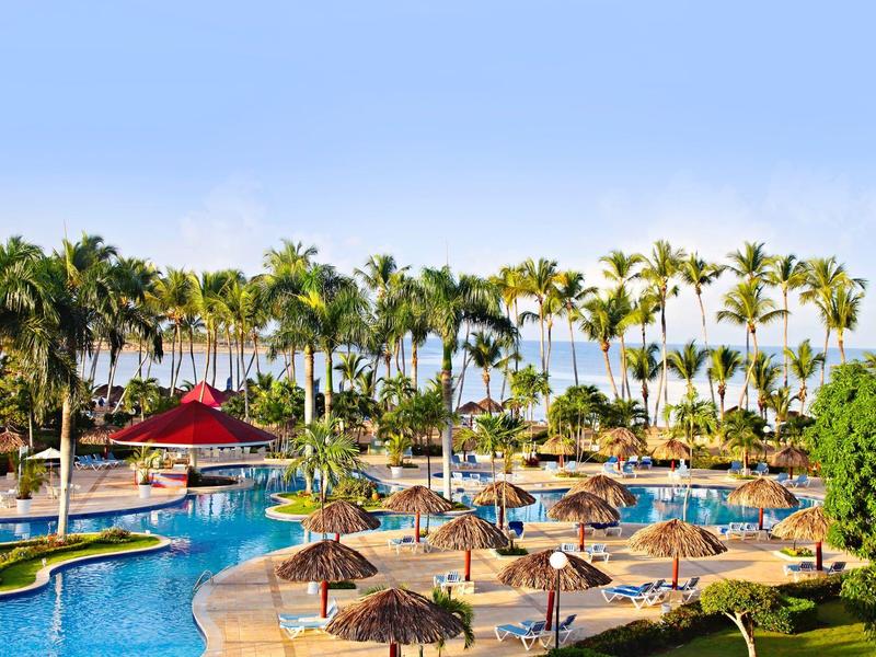 Duży obszar basenu z palmami, parasolami i niebieskimi leżakami pod czystym niebem