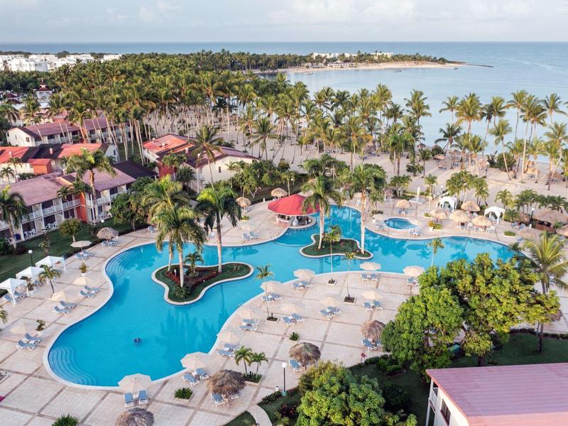 Duży basen hotelowy z palmami i leżakami obok białej piaszczystej plaży