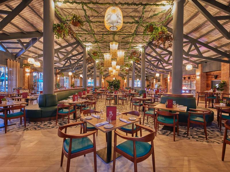 Amplio comedor de restaurante rústico de hotel con mesas de madera, sillas y abundante decoración vegetal.
