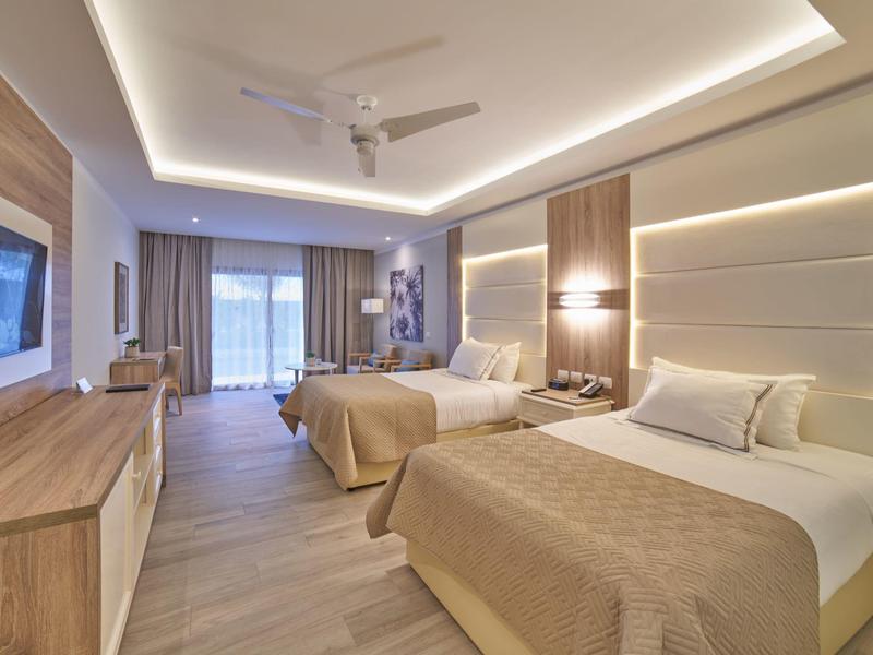 Habitación de hotel luminosa con dos camas, muebles de madera e iluminación moderna.