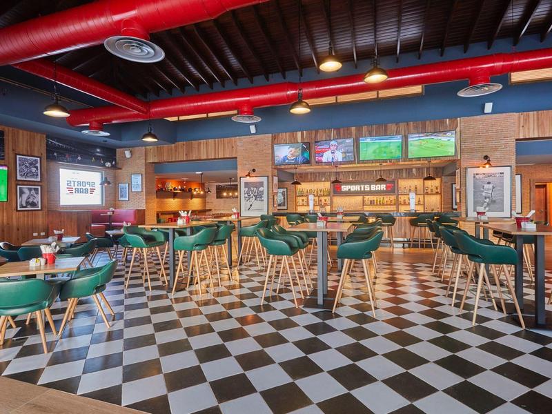 Sala de bar moderna con taburetes verdes y suelo ajedrezado en blanco y negro.