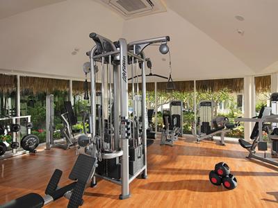 Helles Fitnessstudio mit modernen Geräten und Holzboden, umgeben von großen Fenstern mit Blick ins Grüne.