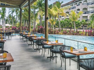 Buitenrestaurant met tafels naast een zwembad en palmbomen bij een hotel.