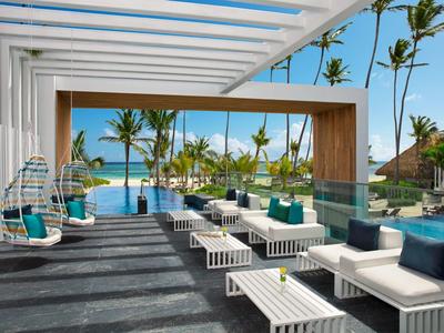 Moderne buitenruimte met witte zitmeubels, hangstoelen en uitzicht op zwembad en palmbomen.