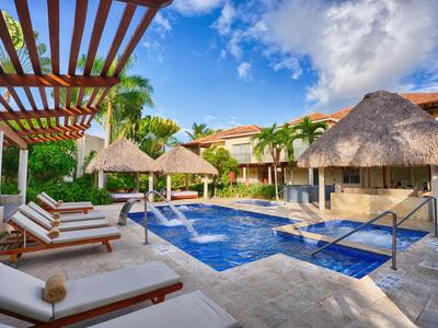 Hotelpool mit Liegestühlen, Palmen und Strohdächern unter blauem Himmel