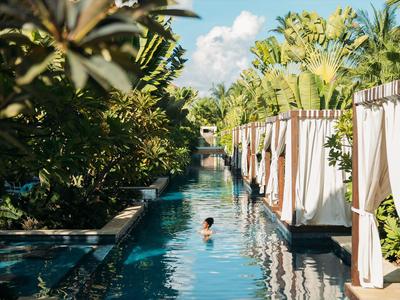 Ein langer Pool mit Pflanzen und weißen Vorhängen, eine Person schwimmt darin.