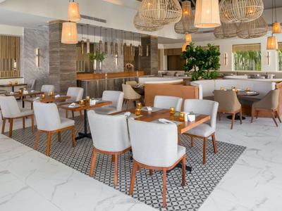 Modernes Hotelrestaurant mit weißen Stühlen und Holztischen auf gemustertem Bodenbelag.