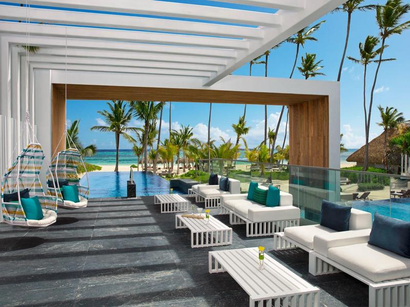 Moderne buitenruimte met witte zitmeubels, hangstoelen en uitzicht op zwembad en palmbomen.
