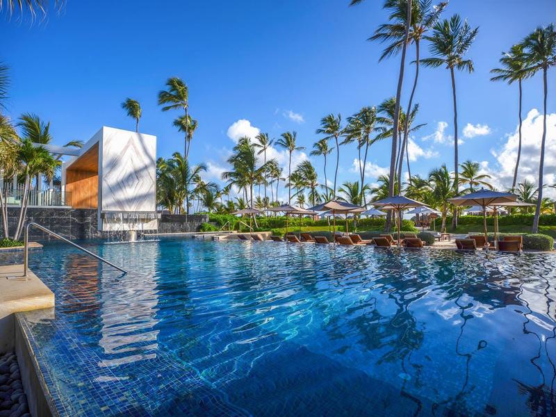 Modernt buitenzwembad met helder blauw water en palmbomen in een tropisch hotel.