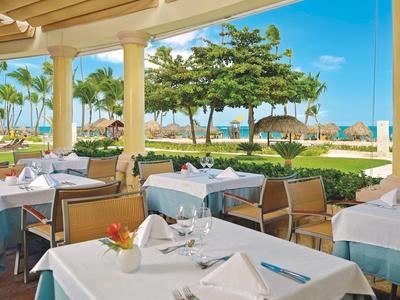 Outdoor restaurant with set tables and view of tropical trees and blue sky.