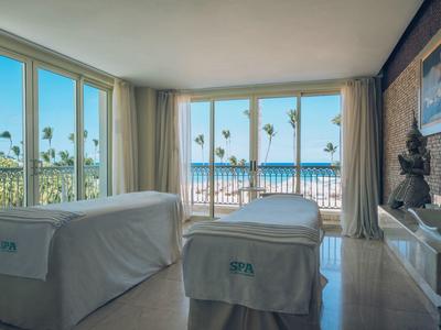 Bright treatment room with two massage tables, large windows, and sea view.