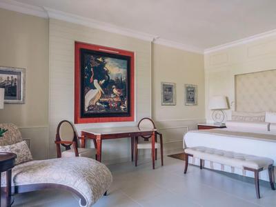 Elegant hotel room with large bed, two chairs, a table, and artwork on the wall.