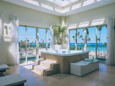 Bright room with hot tub, panoramic windows, and view of palm trees and sea