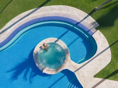 Round swimming pool with integrated hot tub and sunbed in sunlight on a grassy area.