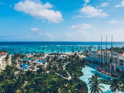 Ośrodek hotelowy z basenami, palmami i widokiem na niebieskie morze pod błękitnym niebem.