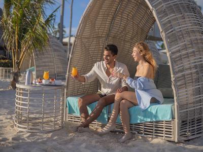 Couple sitting under a beach cabana drinking orange juice on the sand.