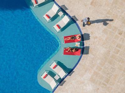 People relax on sunbeds by a hotel pool in sunny weather.