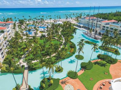 Vista di un resort tropicale con ampie piscine, palme e accesso diretto alla spiaggia.