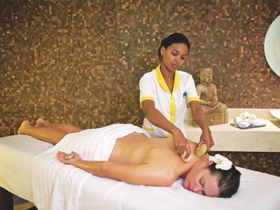 Woman receiving neck massage in relaxed spa setting with brown textured wall and decoration.