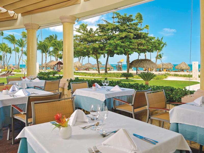 Outdoor restaurant with set tables and view of tropical trees and blue sky.