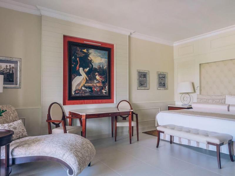 Elegant hotel room with large bed, two chairs, a table, and artwork on the wall.