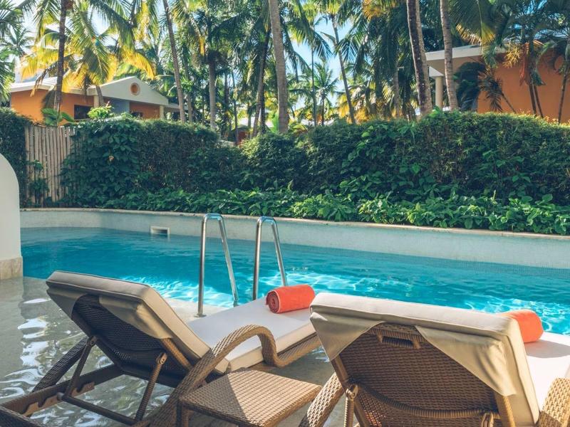 Two lounge chairs with red towels beside a pool with palm trees and shrubs in the background.
