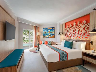 Camera d'hotel luminosa con letto grande, opera d'arte colorata e vista sul mare dalla finestra.