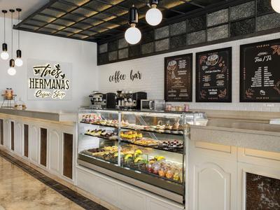 Bancone moderno di caffetteria con vetrina illuminata, parete con logo e lampade a sospensione decorative.