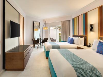 Modernes Hotelzimmer mit zwei Doppelbetten, buntem Wanddesign und großem Fenster.