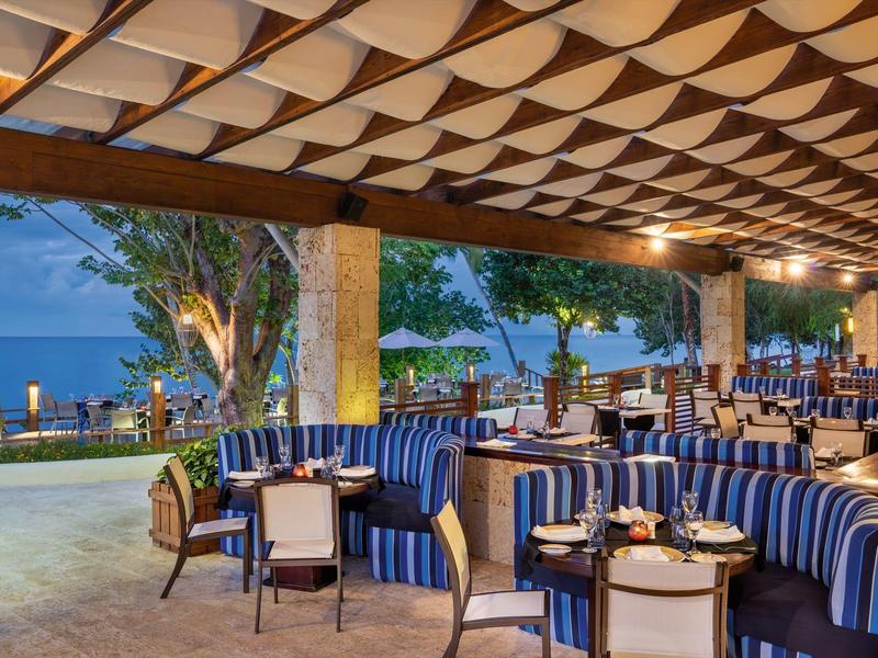 Zadaszona restauracja z niebiesko paskowanymi miejscami do siedzenia i widokiem na morze o zmierzchu.