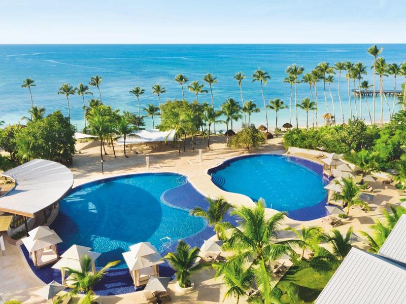 Luksusowy basen przy plaży z palmami i leżakami pod niebieskim niebem.