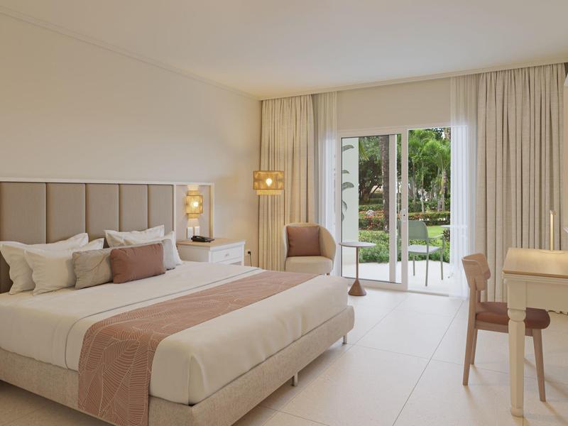 Helles, modernes Schlafzimmer mit großem Bett, Sitzbereich, Schreibtisch und Blick auf Garten.