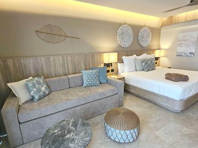 Modernes Hotelzimmer mit Doppelbett, Sofa, Teppichen und dekorativen Wandobjekten in sanften Farben.