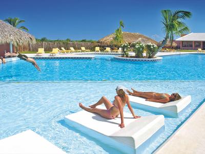 Zwei Personen entspannen auf Liegen am Pool eines sonnigen Resorts mit Palmen.