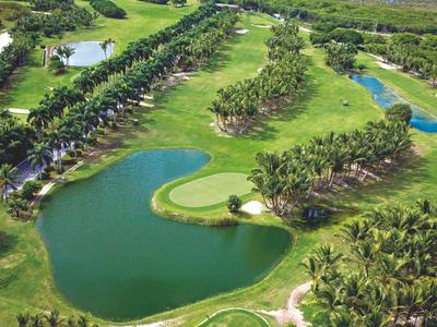 Blick auf einen Golfplatz mit mehreren Wasserhindernissen und Palmen in einer tropischen Umgebung.