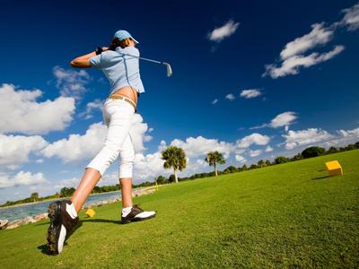 Golfer schlägt Ball auf grünem Golfplatz unter blauem Himmel mit weißen Wolken.